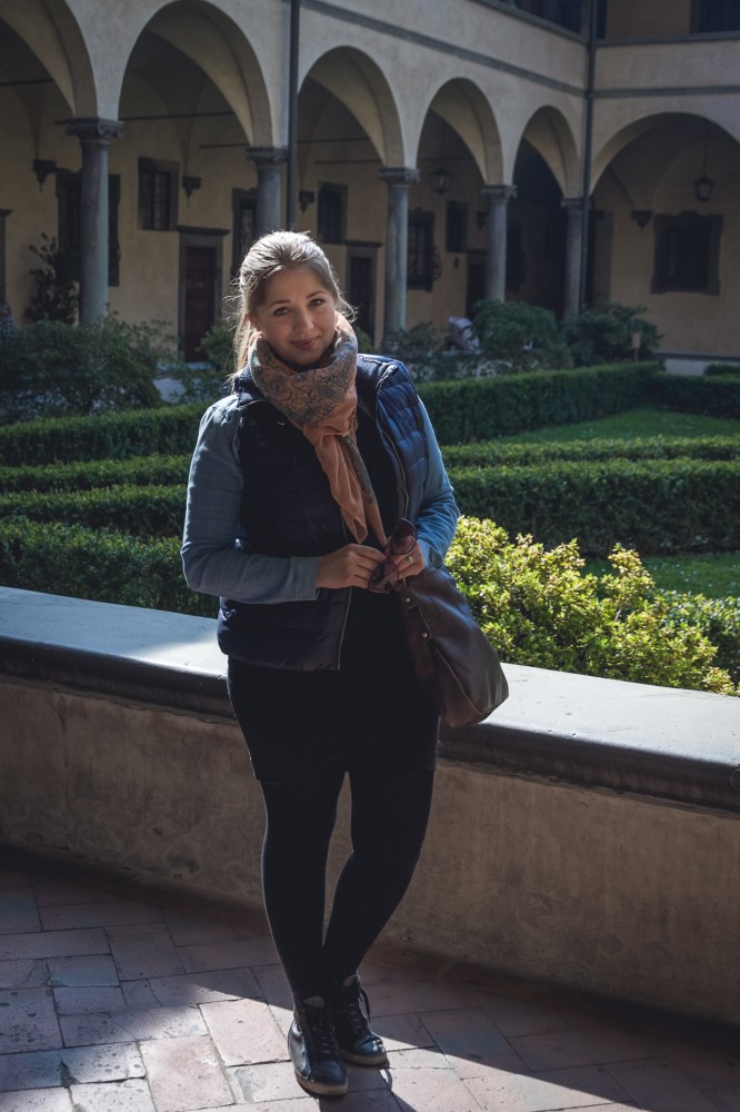 Julika's casual sightseeing look in Florence, Italy, in March: Black mini skirt and tights combined with a chambray shirt and a down vest and sneakers. 